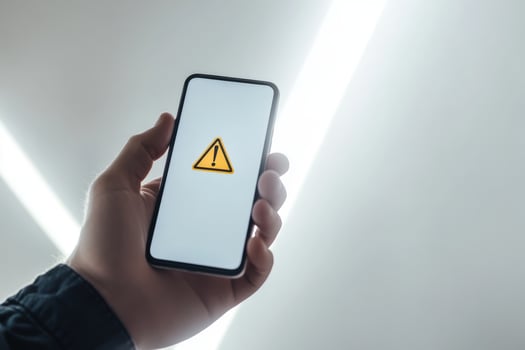 A hand grips a smartphone showing a warning sign, highlighting the importance of caution in financial decisions, investments, and awareness of potential economic risks that could cause harm photo