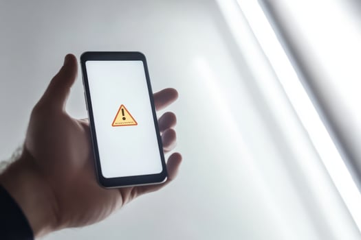 A smartphone shows a warning icon about potential financial risks. Stay alert against fraud and downturns to protect your money from various threats endangering your financial safety photo