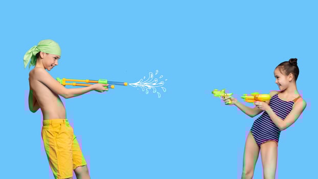 Family battle. Little brother and sister playing at pool, shooting each other with water guns, blue studio background photo