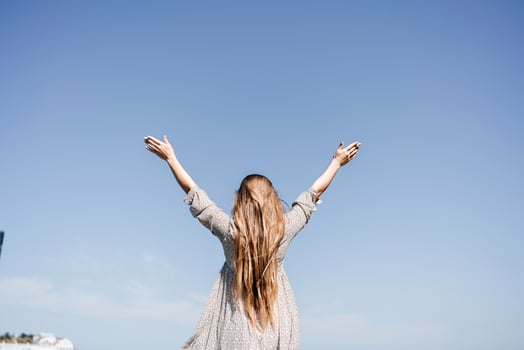A woman with long hair is standing on the beach, looking up at the sky. She is wearing a dress and she is happy. photo