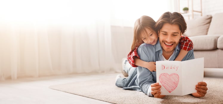 Happy father reading greeting self-made card while bonding with daughter on floor at home, free space photo