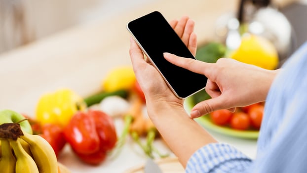 A woman uses her smartphone in a kitchen, with fresh produce in the background. photo