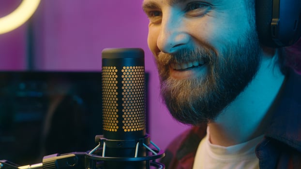 Happy Caucasian man carefree gamer male guy influencer in headphones cyber sport radio blogger talking in microphone stream online on Internet broadcast content home neon popular streamer speak smile photo