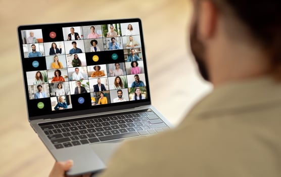 A man is seated in front of a laptop, where a screen displays a call with multiple people. He appears focused and engaged as he interacts with the group virtually. photo