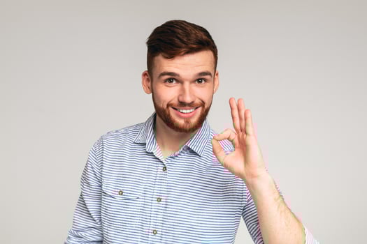 It is ok. Handsome guy wearing casual shirt showing okay gesture and smiling on grey studio background photo