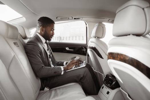 Black businessman working on his laptop in the backseat of a luxury car. He is dressed in a suit and tie, and is focused on his work. The car is spacious and comfortable, with white leather seats photo