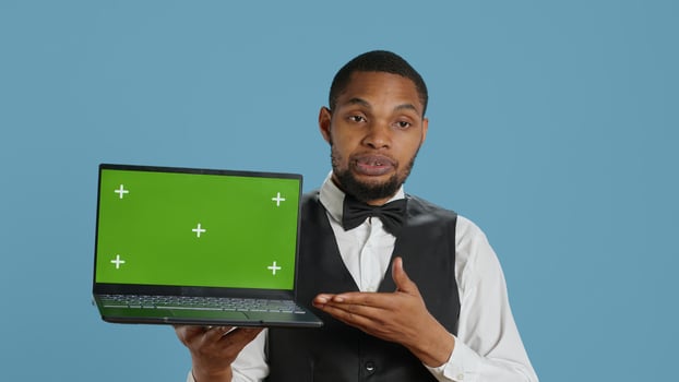 Doorkeeper bellboy holding a laptop with green screen in studio, presenting isolated chroma key display while he works in hospitality industry at a five star hotel. Professional staff. Camera A. photo