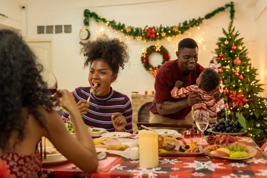 A joyful family gathers around the dinner table celebrating Christmas. The father, dressed in a Santa hat, gives a gift to the child, while everyone smiles with warmth and festive decorations. photo
