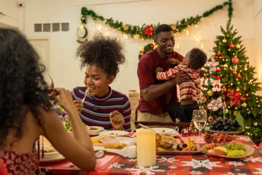 A joyful family gathers around the dinner table celebrating Christmas. The father, dressed in a Santa hat, gives a gift to the child, while everyone smiles with warmth and festive decorations. photo