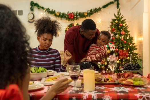 A joyful family gathers around the dinner table celebrating Christmas. The father, dressed in a Santa hat, gives a gift to the child, while everyone smiles with warmth and festive decorations. photo