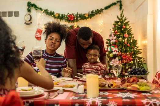 A joyful family gathers around the dinner table celebrating Christmas. The father, dressed in a Santa hat, gives a gift to the child, while everyone smiles with warmth and festive decorations. photo