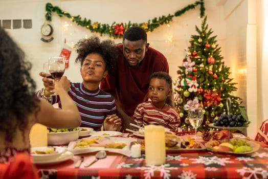 A joyful family gathers around the dinner table celebrating Christmas. The father, dressed in a Santa hat, gives a gift to the child, while everyone smiles with warmth and festive decorations. photo