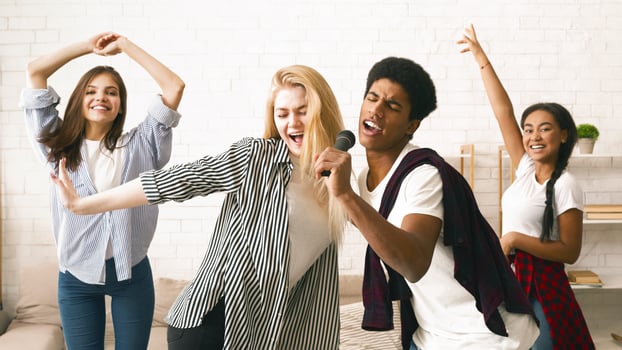 A vibrant group of four multiethnic friends are engaging in a lively karaoke session, dancing and clapping, caught in a moment of joyous entertainment in a well-lit, cozy room. photo