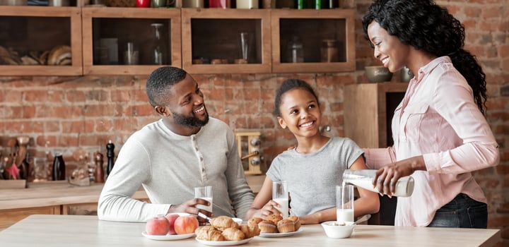 Calcium daily dose. Beautiful black woman pouring milk for her family, copy space photo