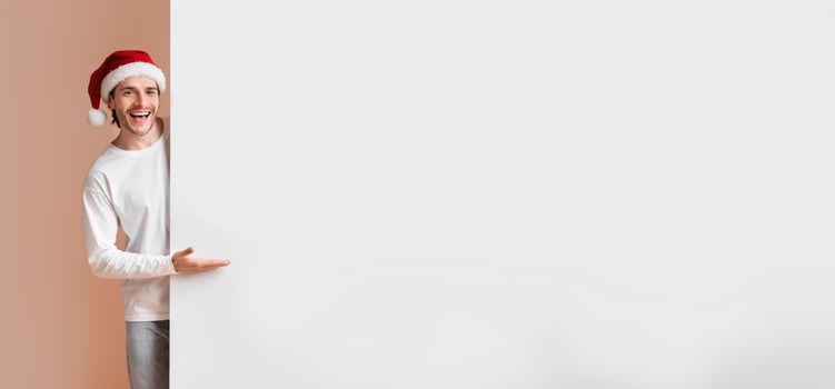 Cheerful Interracial Couple In Santa Hats Holding And Indicating At White Advertisement Board For Your Text, Yellow Background photo