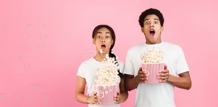 Scary movie. Frightened couple throwing popcorn over pink background photo