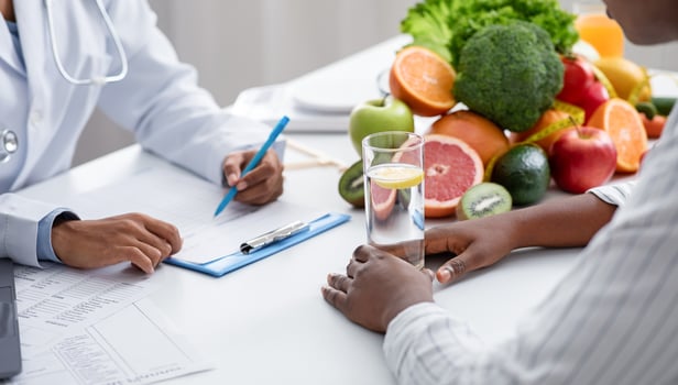 Detox concept. Afro woman patient of nutritionist drinking lemon water while doctor taking notes, close up photo