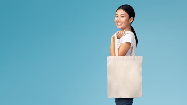 Ecology Concept. Asian Girl With White Eco Bag Smiling At Camera Standing On Blue Studio Background photo