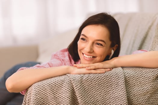 Enjoy Song. Portrait of beautiful pensive lady in headphones lying on sofa and listening to music at home, copyspace photo