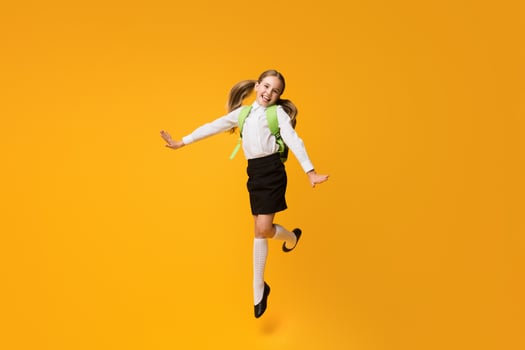 Happy Back-To-School Concept. Gladful Little Schoolgirl Jumping Over Yellow Background In Studio. Copy Space photo