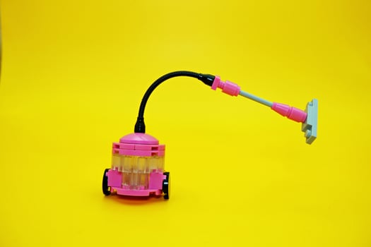 Mini vacuum cleaner toy assembled from plastic blocks. Vacuum cleaner toy isolated on yellow background. photo