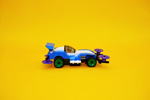 blue racing car assembled from plastic blocks. toy car isolated on yellow background photo