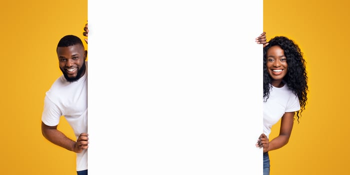 Black Girl And Guy Holding White Advertising Board, yellow studio background, panorama photo