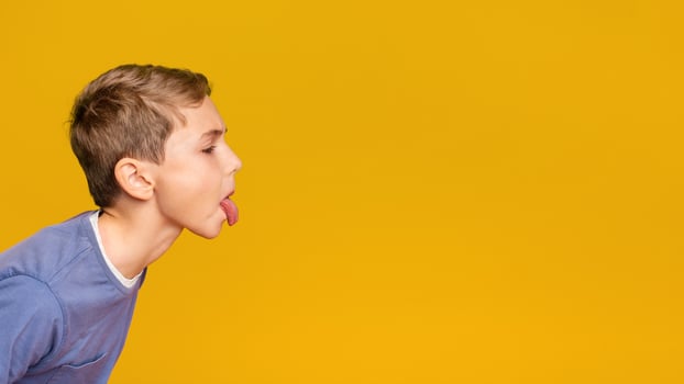 Little boy teasing someone, showing tongue and making face at free space aside, orange background photo