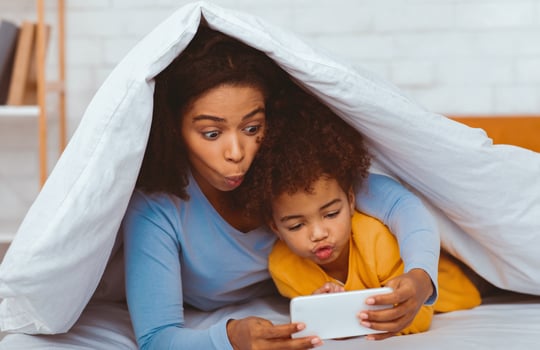 African Mom And Little Girl Playing Mobile Games On Smartphone Lying In Bed Having Fun Together. Selective Focus photo
