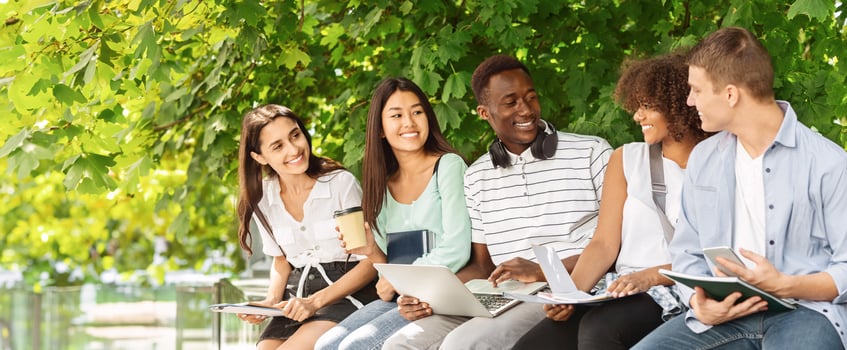 Group of multicultural students sitting in the courtyard of university, chatting and studying together, preparing for lessons photo