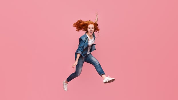 Redhead girl screaming and jumping in air on pink studio background photo