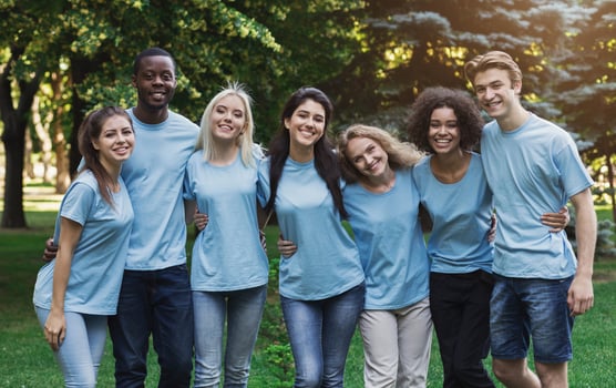 Group of happy young diverse volunteers embracing at park, ready for work, copy space photo
