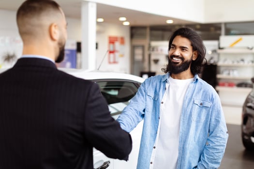 Two men are standing in a car showroom, shaking hands in agreement. The men appear serious and focused on finalizing a deal for a car purchase photo