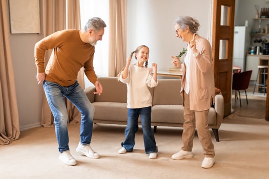A young girl is gleefully dancing with her grandparents in the warmth of their living room, sharing a special moment of laughter and fun, all expressing happiness and the strong bond of family. photo