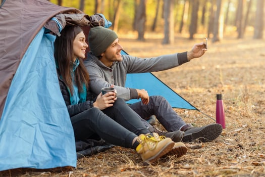 Couple of young tourists taking selfie on smartphone in camping tent in autumn forest, copy space photo