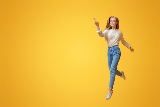 Look there. Cheerful teen girl jumping and pointing aside on copy space over orange background photo