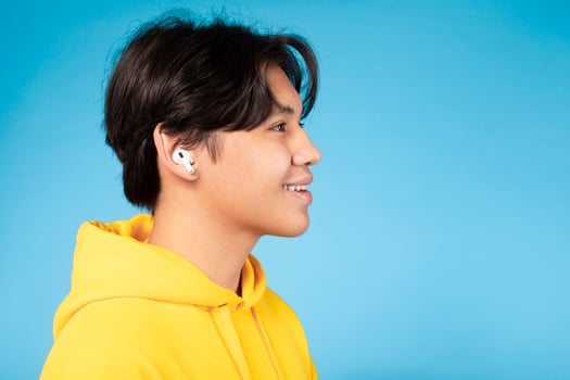 Asian young guy is shown wearing ear buds on his ears, immersed in listening to music. He appears focused on the music playing through the ear buds, copy space photo