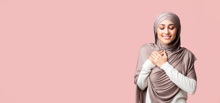 Gratitude concept. Thankful muslim girl in hijab keeping both palms on chest, expressing appreciation over pink studio background with copy space photo