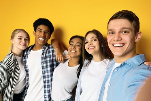 A cheerful group of five multiethnic teenagers is seen posing closely together in a friendly embrace, take selfie on yellow studio background photo