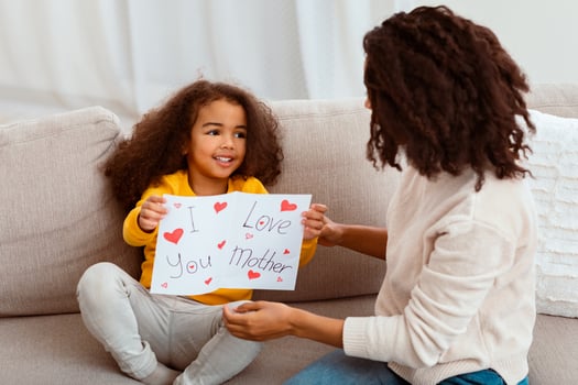 Little African American Daughter Congratulating Mother Giving Self-Made Greeting Card On Holiday At Home. Happy Mother's Day Concept photo