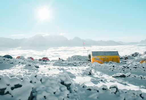 Climber surrounded by tents in Bethlemi hut base camp above clouds on sunny morning. Acclimatization and mountaineering concept. Climbing Mount Kazbek. Kazbegi municipality famous destination photo