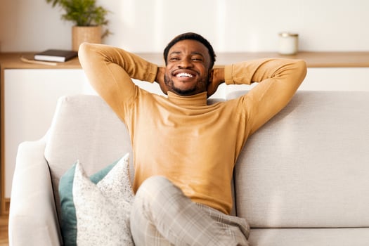 Relaxed African American Man Resting Sitting On Couch Holding Hands Behind Head At Home. Enjoying Weekend. Free Space photo