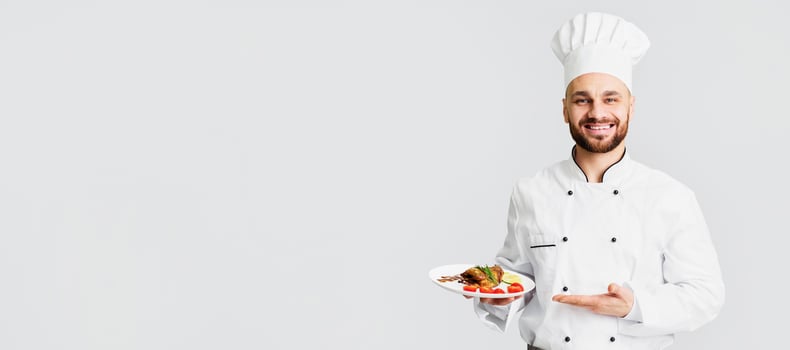 Smiling Male Chef Serving Chicken Dish Holding Plate Standing On Gray Background. Selective Focus photo