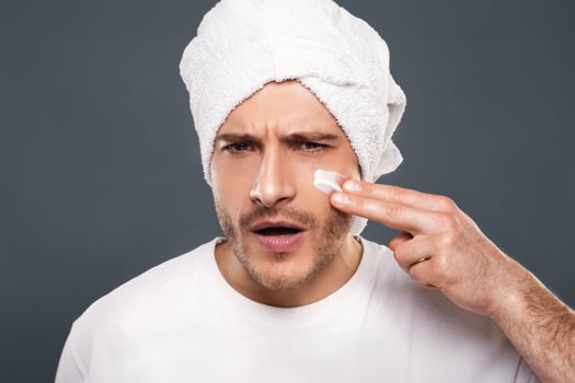 Pampering concept. Handsome man putting cream on his cheeks like warrior, having fun with towel on head photo