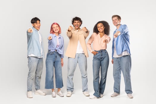 A group of five diverse friends, all smiling and pointing at the camera, are standing in front of a white background in a studio setting. photo