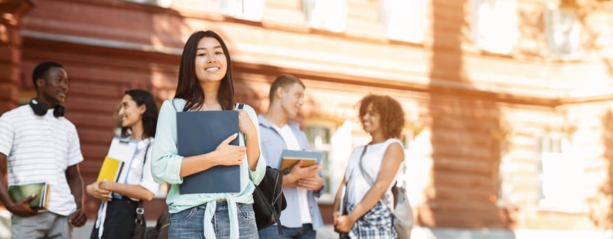 Loans For Education Concept. Portrait Of Happy Asian Student Girl Posing Outdoors In Campus With Her Classmates And University Building On Background photo