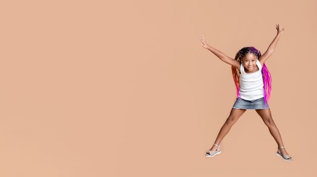 Like a star. Cute little african american girl jumping with her hands up over yellow studio background with copy space photo