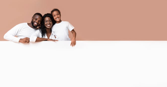 Offer for families. Smiling african american parents and daughter leaning on blank white board with free space for advertisement photo
