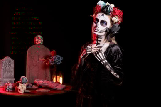 Woman holding black rose participating at Dia de los Muertos party, preserving cultural traditions between generations. Eerie lady with flower wearing la Catrina costume to celebrate Mexican culture photo