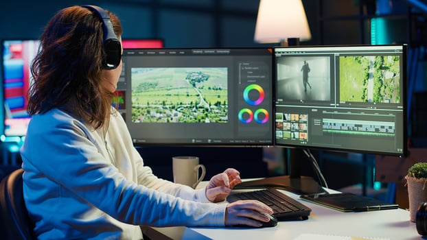 Videographer working on film montage, editing color grading and listening music. Post production studio worker manipulating raw footage, doing adjustments, wearing headphones, camera A photo